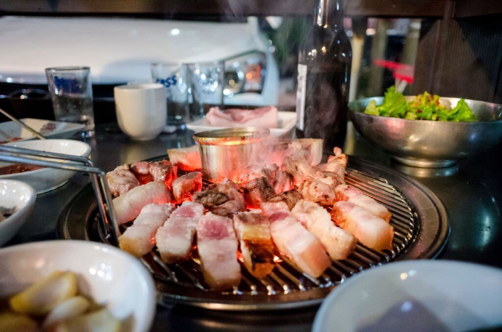 Thịt ba chỉ nướng BBQ (Samgyeopsal) trên vỉ than hồng cùng các món ăn kèm tại nhà hàng Hàn Quốc.