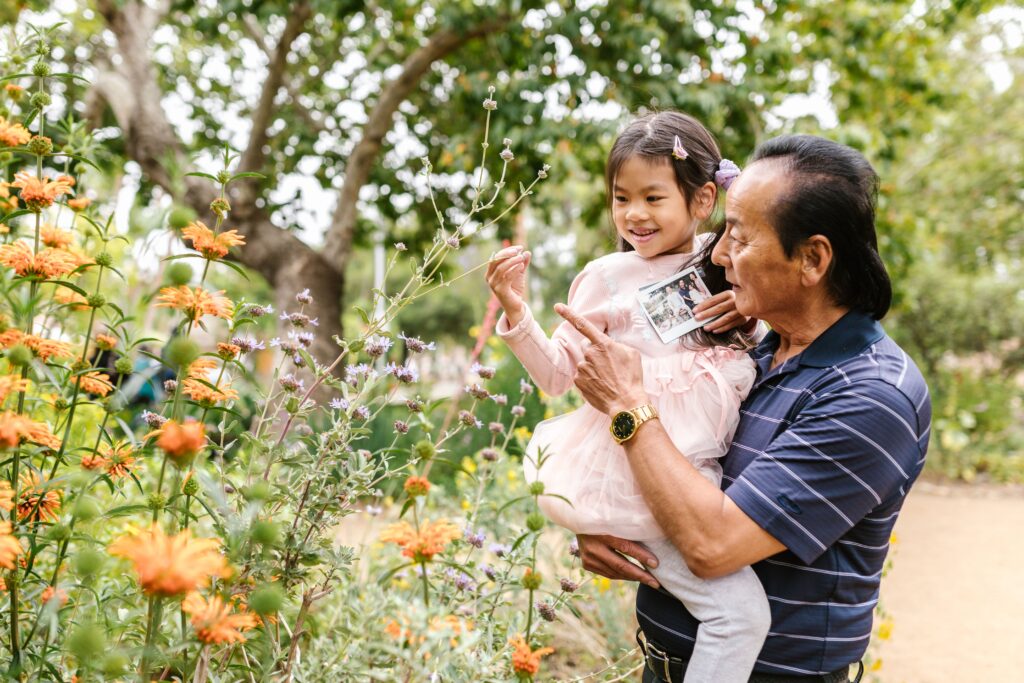 Hình ảnh người ông bế cháu gái ngắm hoa trong vườn, thể hiện sự gắn kết tình thân trong chuyến du lịch đa thế hệ.